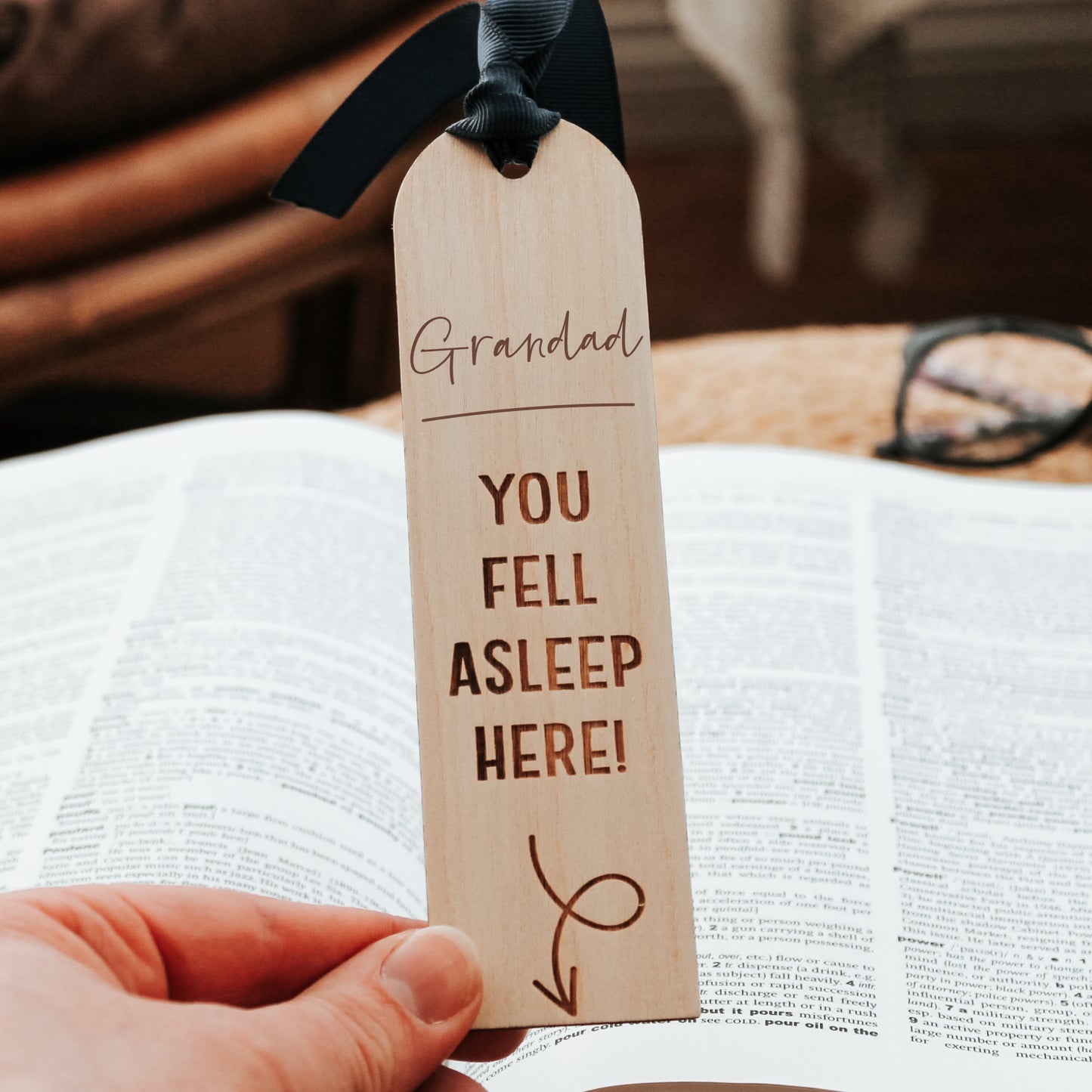 Playful wooden bookmark engraved with "Grandad you fell asleep here" message pointing to a book below. Finished with a blue ribbon, it's the perfect reminder for book-loving grandfathers.