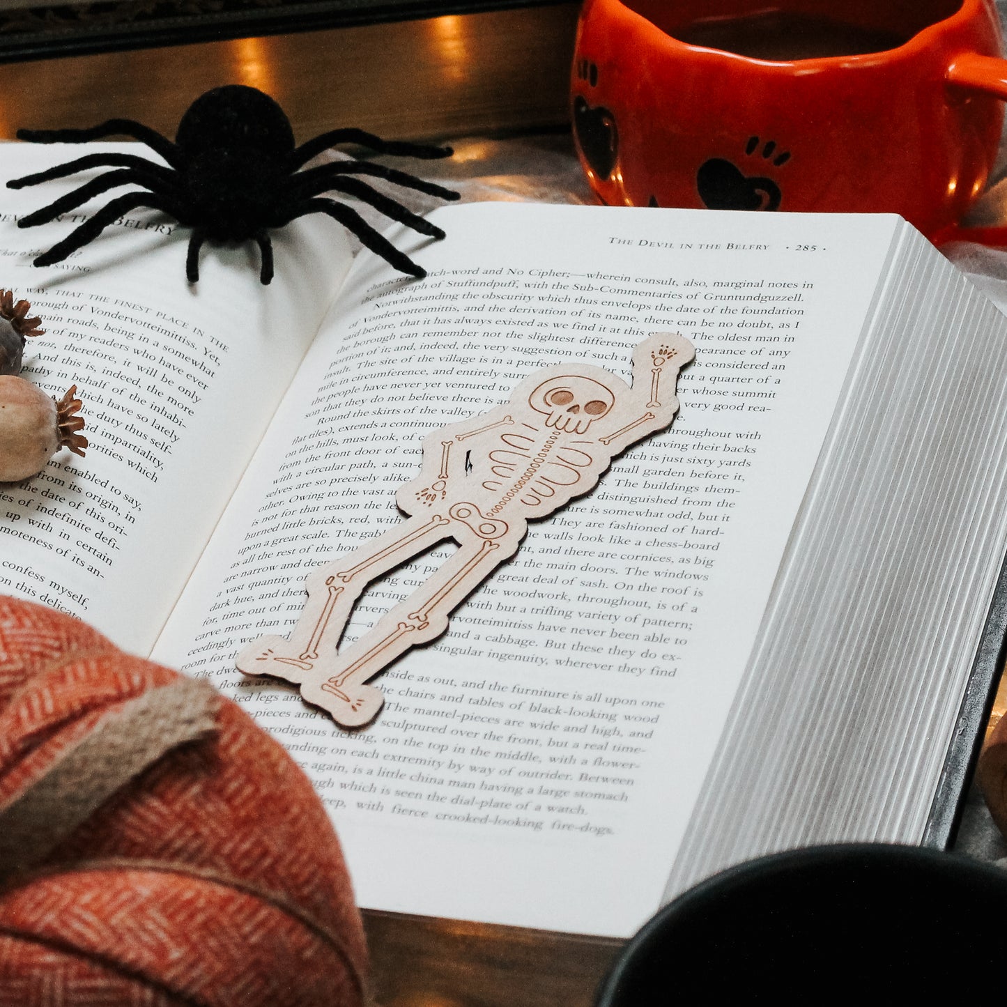 wooden engraved cute skeleton bookmark laying on an open book. surrounded by Halloween décor