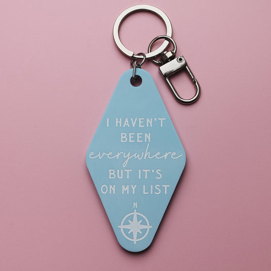 Blue motel style keychain with the quote 'I haven't been everywhere, but it's on my list' on a pink background