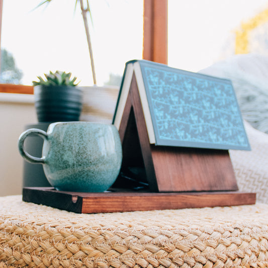 A dark wooden book valet designed to hold a book and a beverage, ideal for relaxing with a good read.