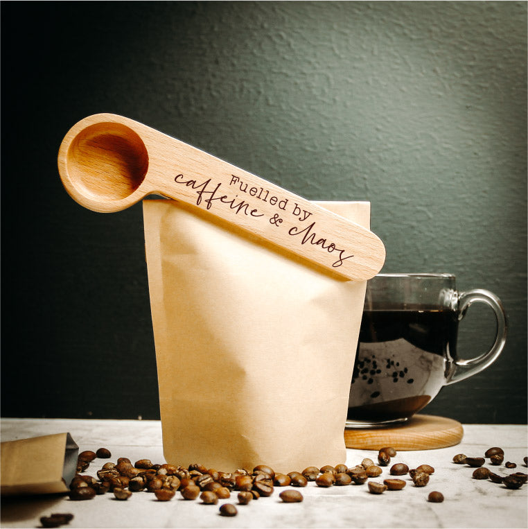 a wooden coffee spoon that is also a clip for your coffee bag engraved with the words fuelled by caffeine and chaos, a perfect gift for the coffee lover