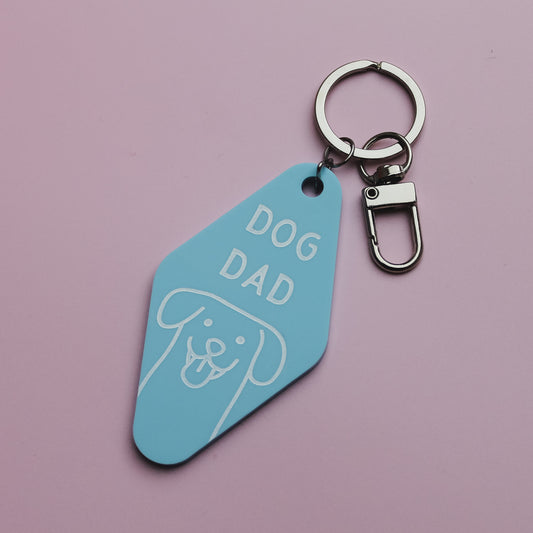 Blue Motel Style keychain tag with 'DOG DAD' text on a pink background