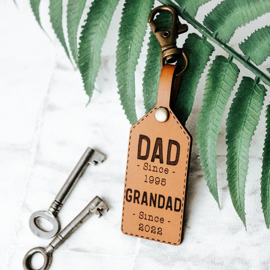 leather keyring with the wording dad since 1995 and grandad since 2022 engraved on it, in a whisky colour. Ideal fatehrs day gift