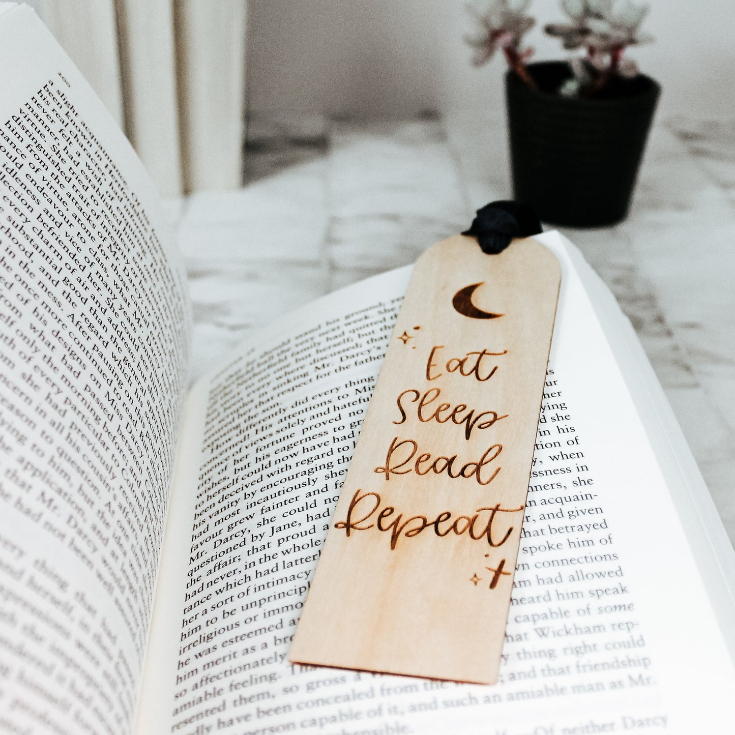 Engraved wooden bookmark with "Eat Sleep Read Repeat" motto, accented by a moonlit scene and a blue ribbon, perfect for bibliophiles who prioritize relaxation and reading.