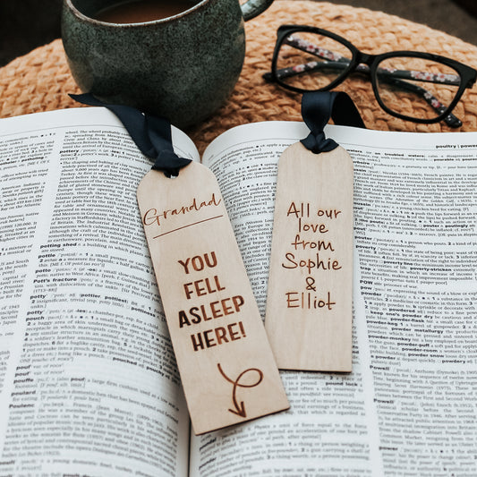 Wooden bookmark engraved with a lighthearted message "Grandad you fell asleep here" with an arrow pointing down to the book. Adorned with a blue ribbon, it's a charming gift for grandfathers who enjoy getting lost in a good story. With the choice of personalisation on the reverse with your own message