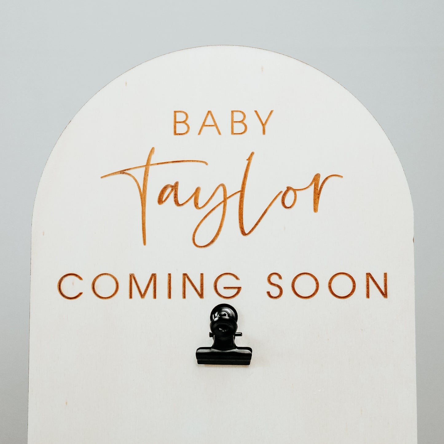 image of the top of the pregnancy announcement sign showing the engraved personalised wording close up. It reads baby taylor coming soon and has a black clip to clip the baby scan image onto
