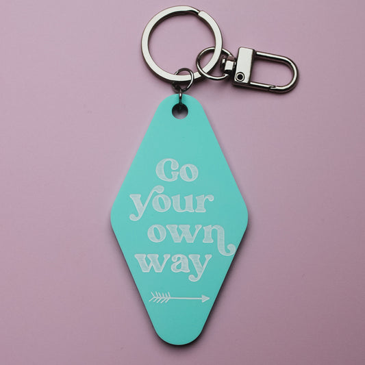 Turquoise motel style keyring with 'Go your own way' text on a pink background