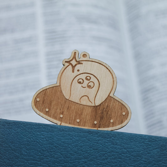 Wooden alien ufo bookmark, peeking out of a closed book.