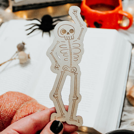spooky skeleton wooden engraved bookmark with quirky spooky skeleton posed in front of a book.