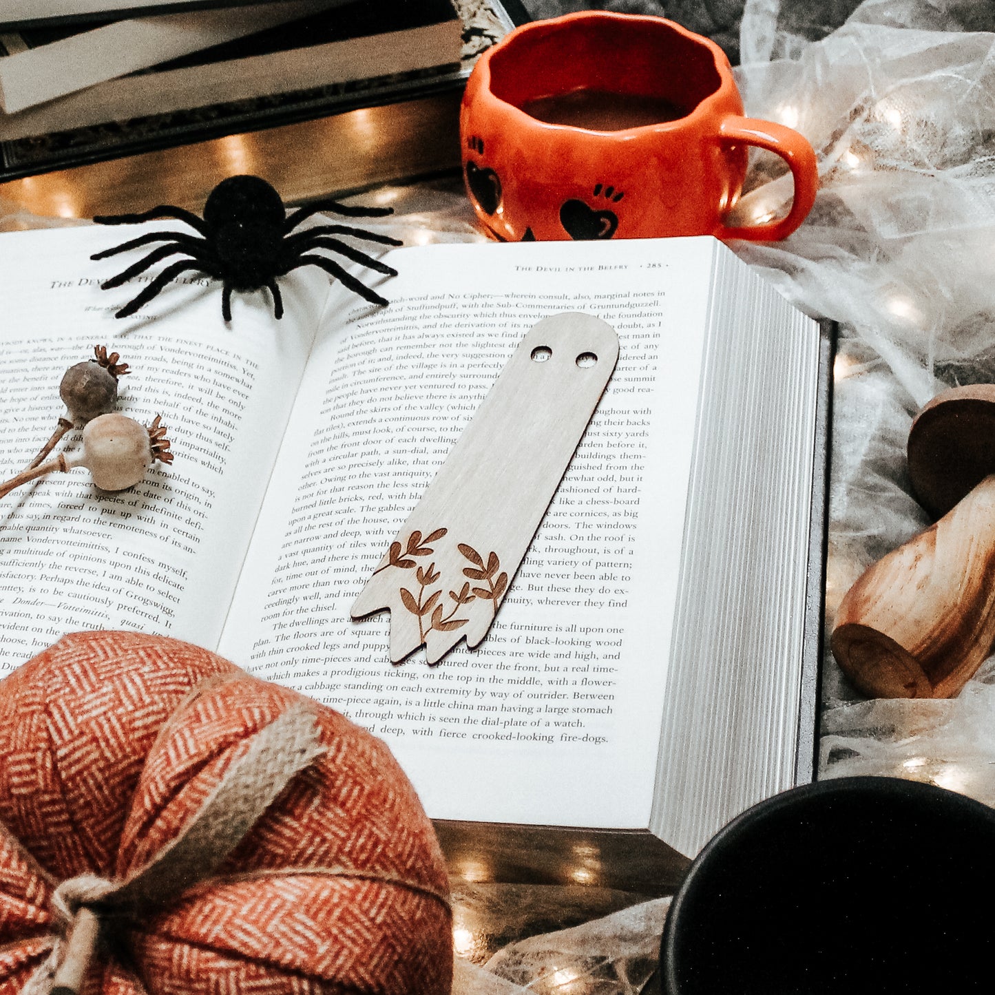 wooden engraved ghost bookmark laying on an open horror book surrounded by Halloween decor