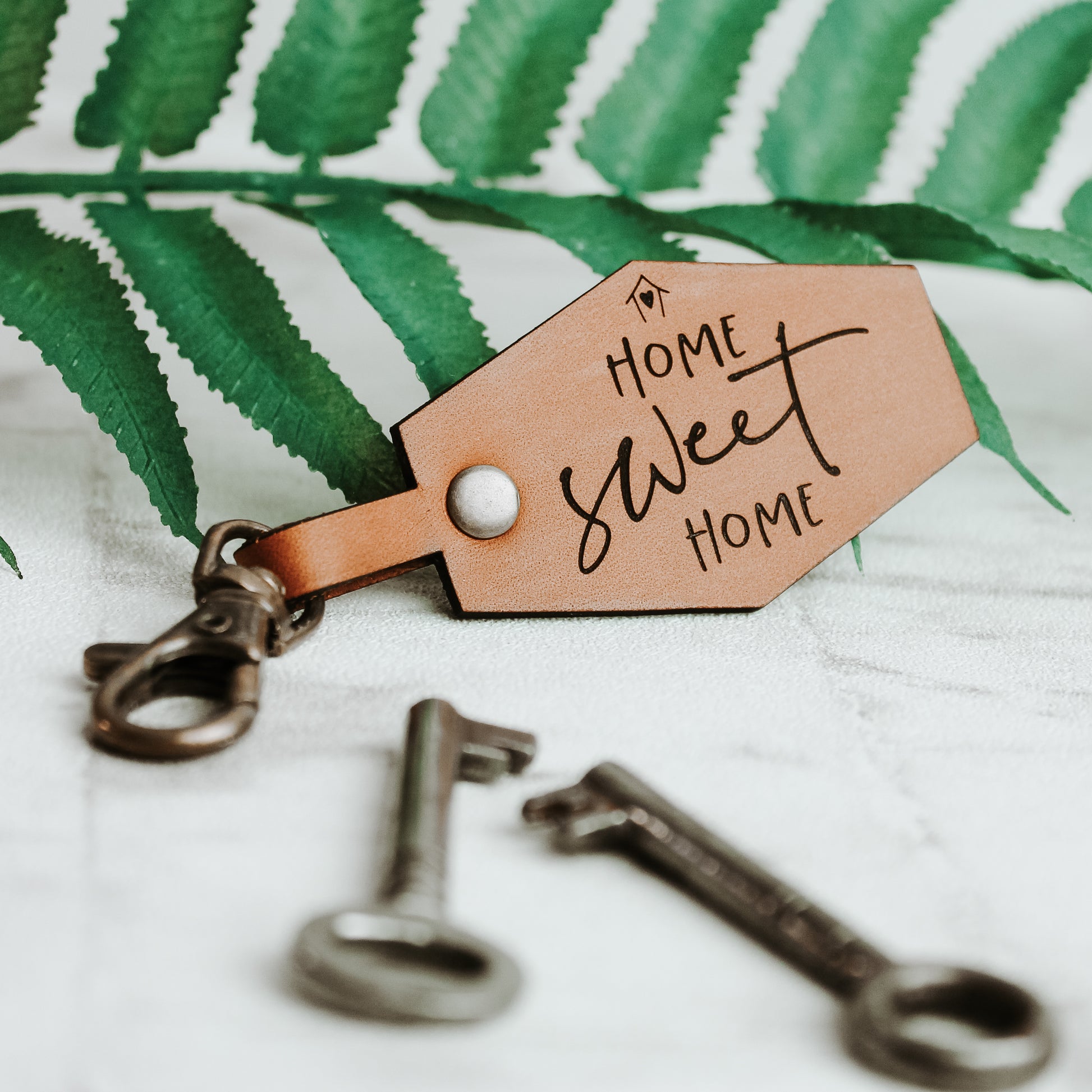 home sweet home keyring in a whisky colour with a swivel clasp, photographed on a fern leaf