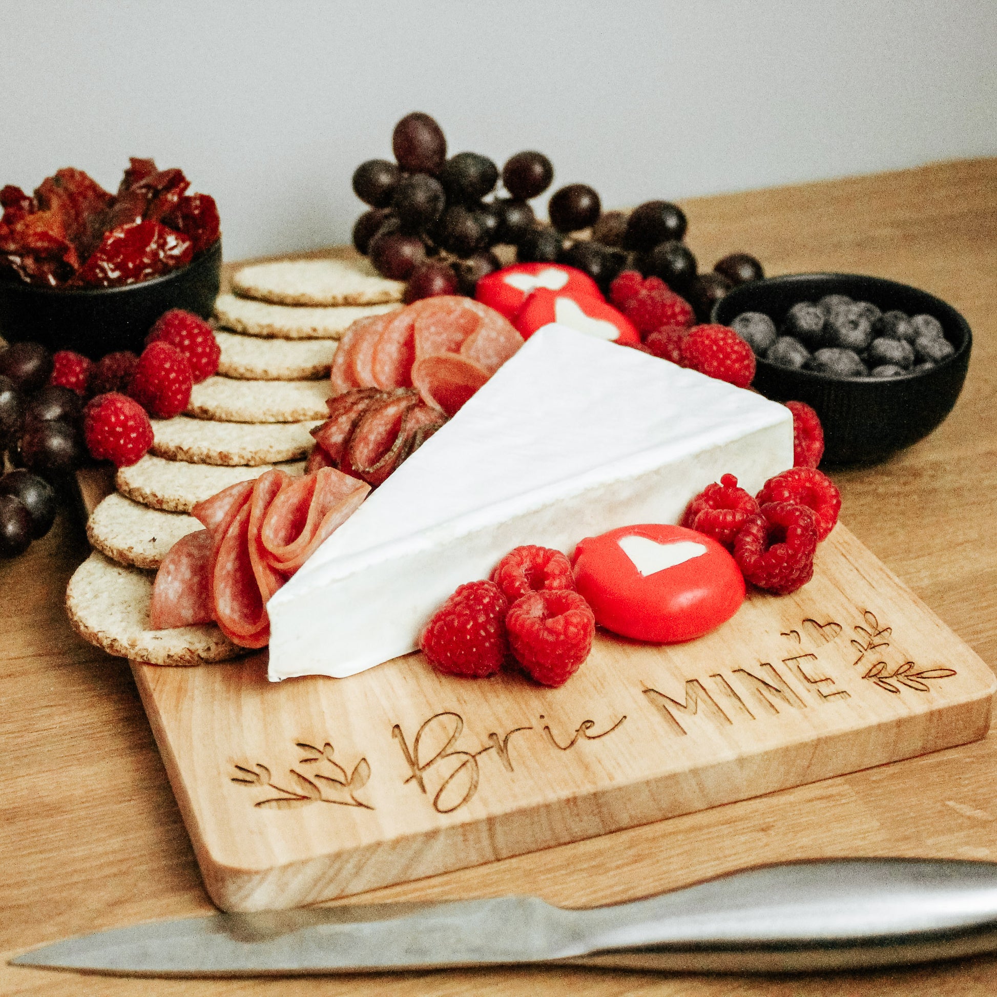 Light wooden chopping board with the words brie mine engraved on it. On the board there is a chesse board selection in a charcuterie board style layout.