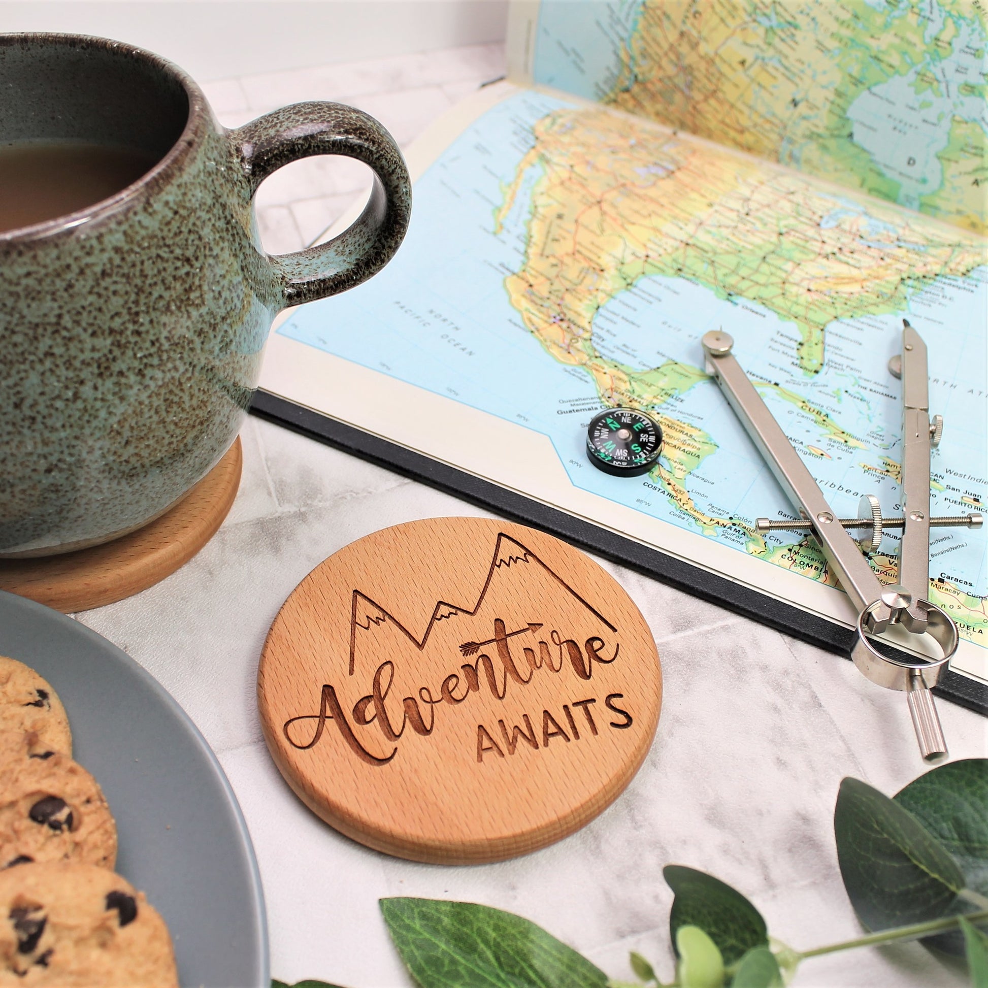 adventure awaits engraved round wooden coaster sitting with a cup of tea and a map