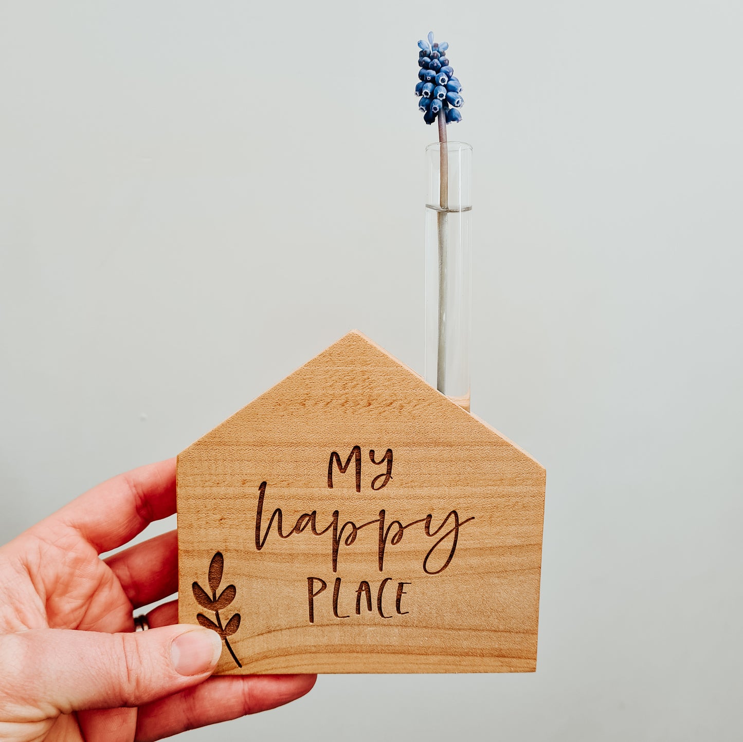 Wooden house shaped vase with test tube holding a single cut flower, engraved with the words my happy place