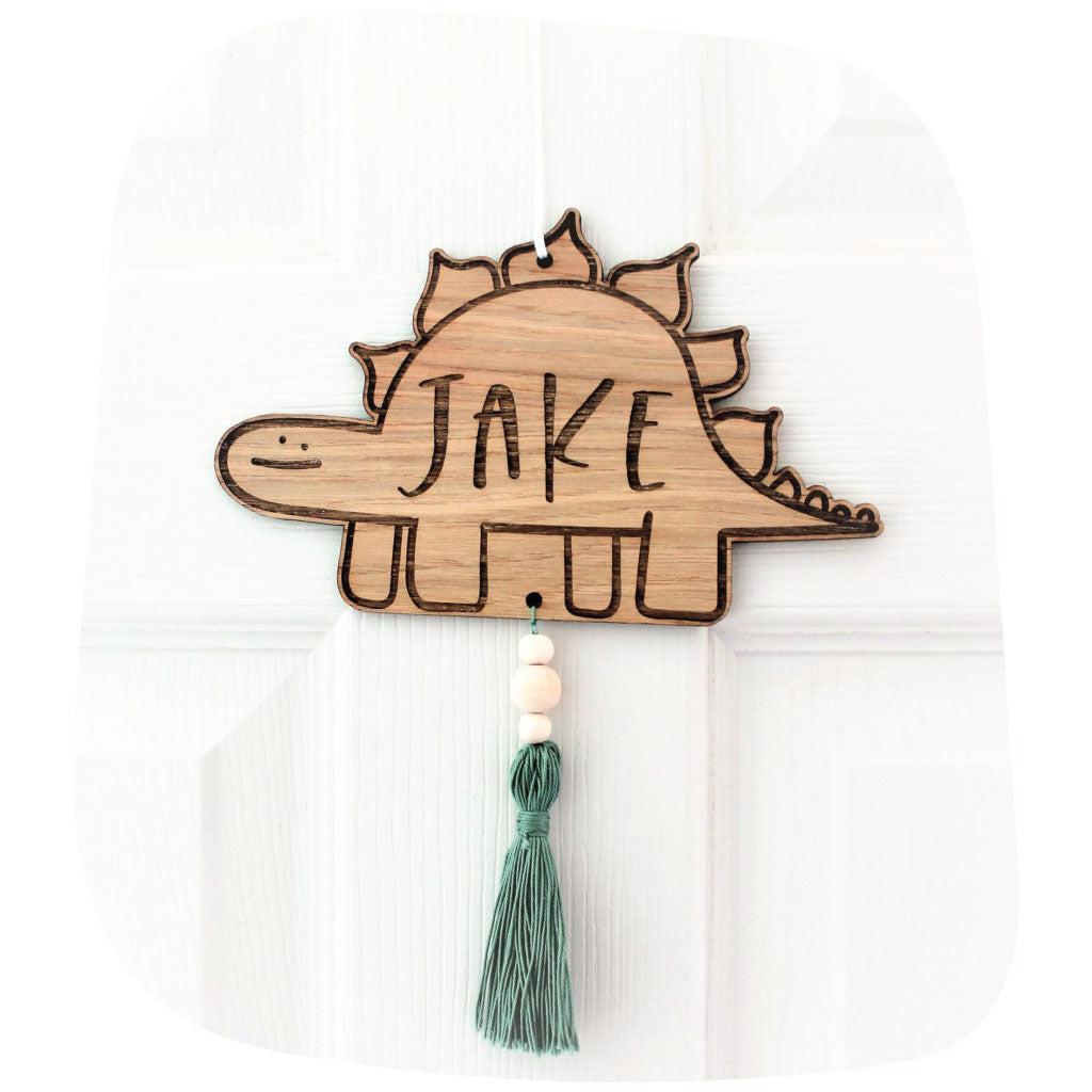 Round Wooden sign engraved with a personalised name hanging on a door with a pink tassel affixed to the bottom 