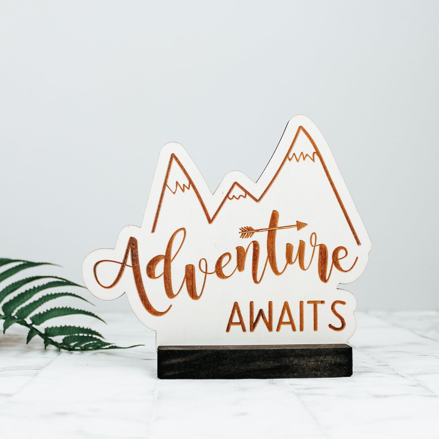wooden engraved playroom or nursery sign with a mountain design and the words adventure awaits in a calligraphy font