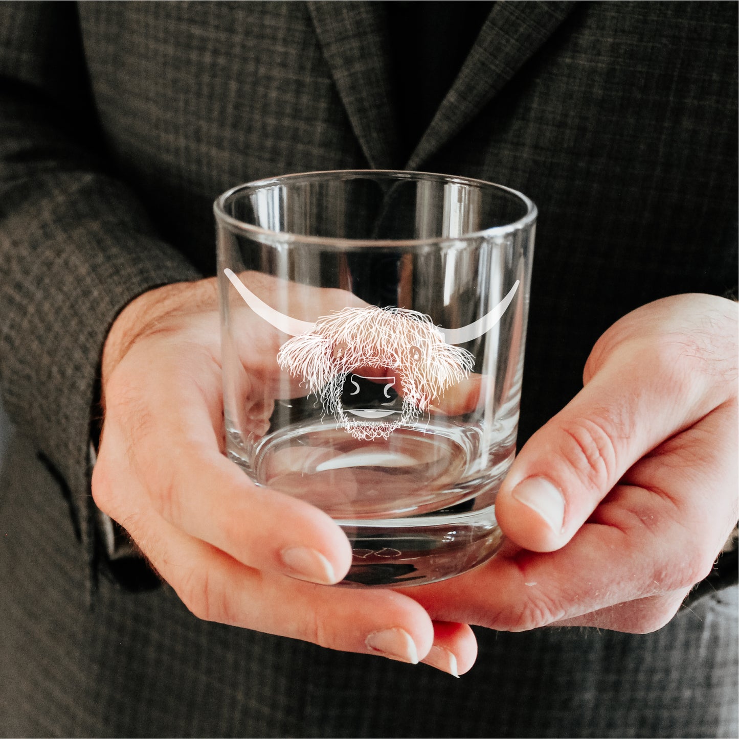 Man holding an engraved whisky glass with a design of a highland cow