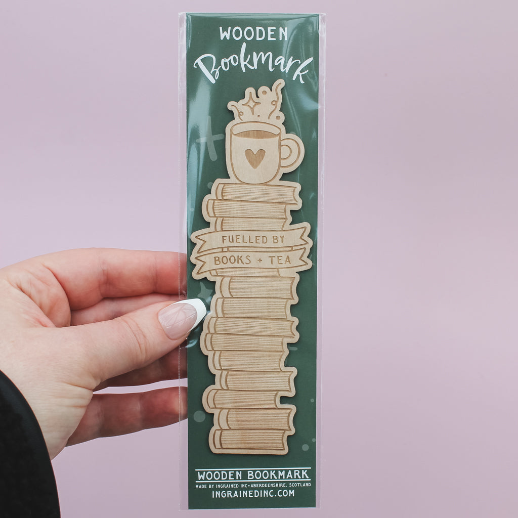 Wooden bookmark with 'Fuelled by Books & Tea' text on a green packaging against a light pink background.