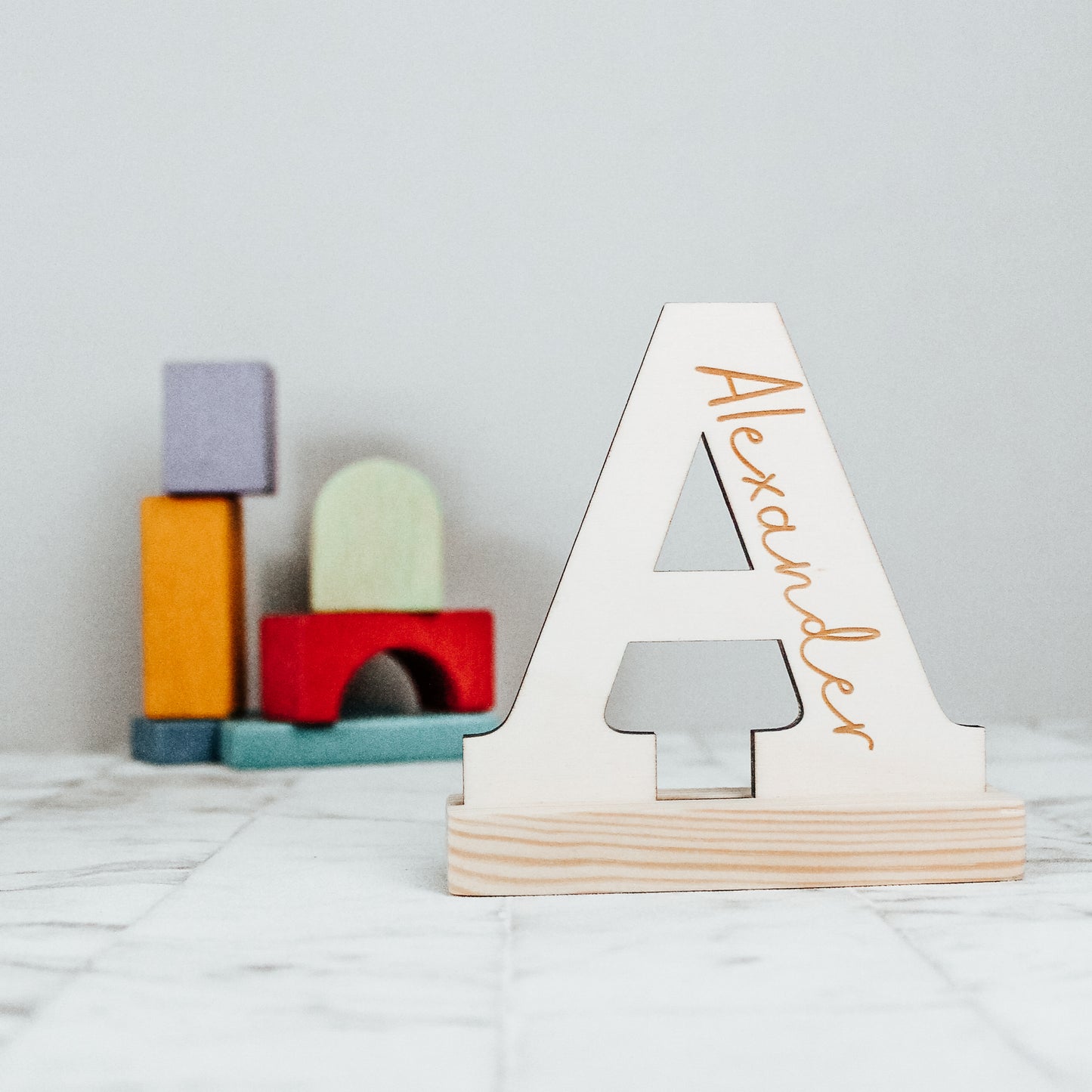 a wooden letter A engraved with the name alexander inside it with a calligraphy font, showing an example of a personalised wooden letter for a child's nursery or playroom 