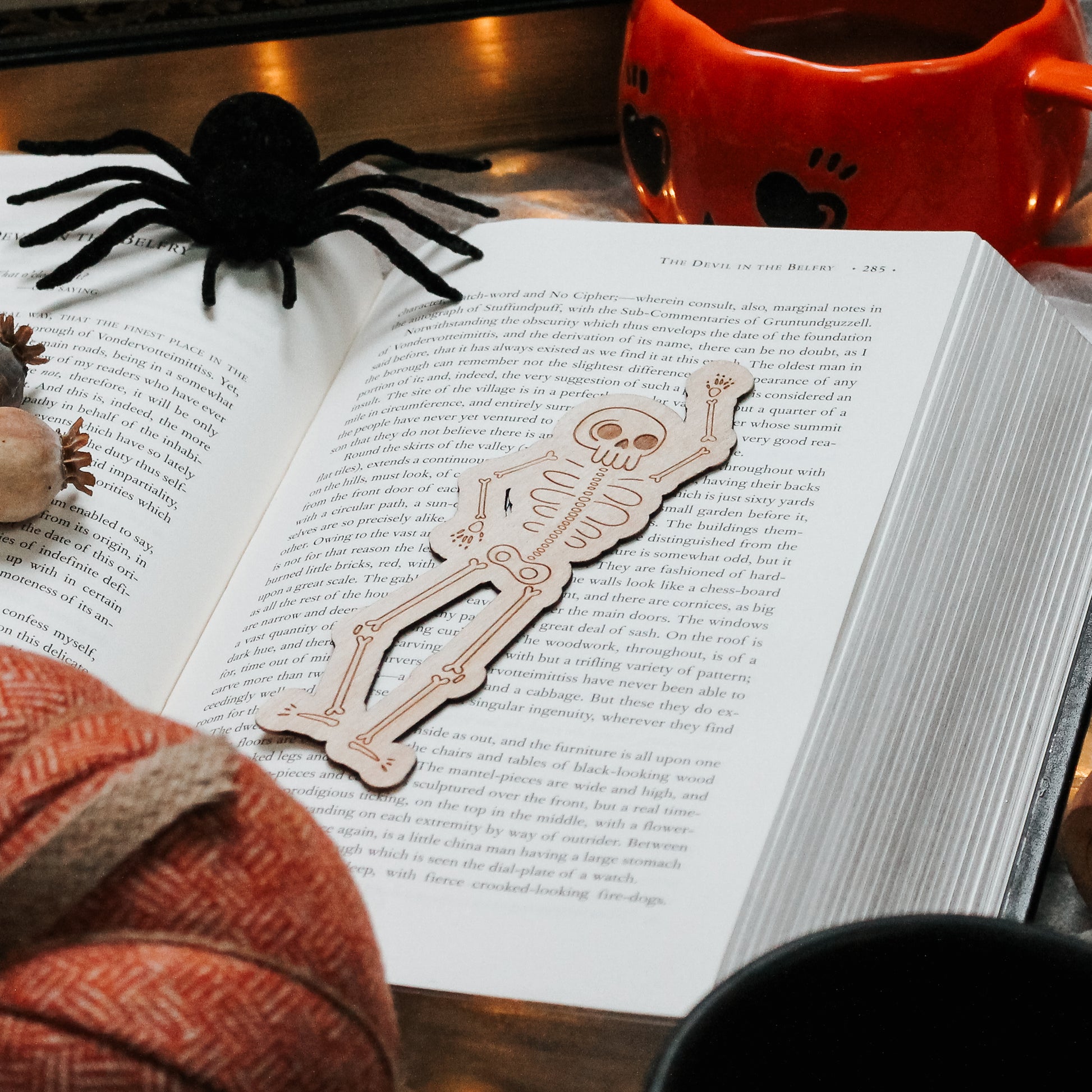 wooden engraved cute skeleton bookmark laying on an open book.  surrounded by Halloween décor