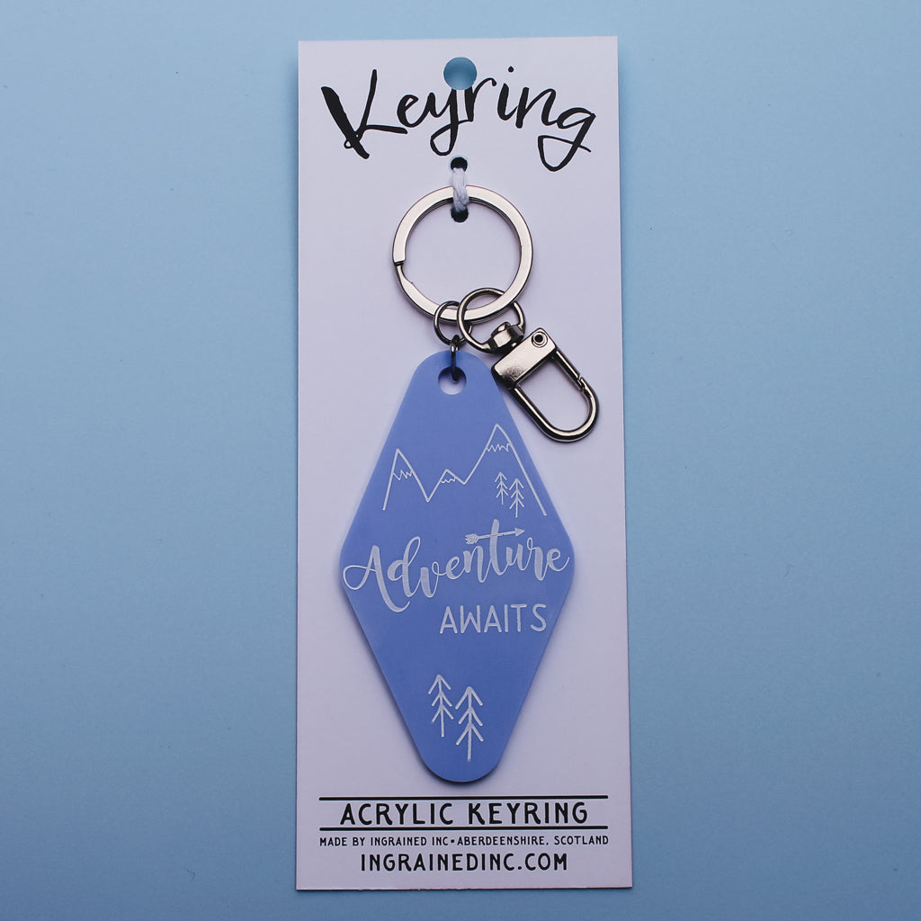 Blue motel style keyring with 'Adventure Awaits' text on a white backing card against a blue background
