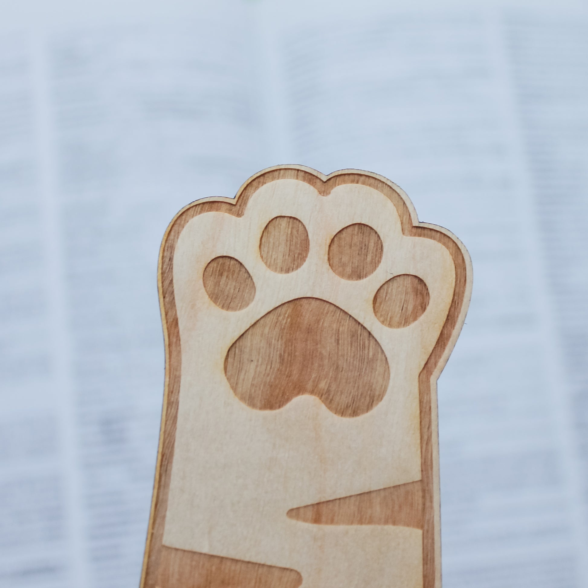 Wooden engraved bookmark shaped like a cat paw print on a light blue background