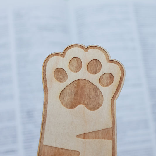 Wooden engraved bookmark shaped like a cat paw print on a light blue background