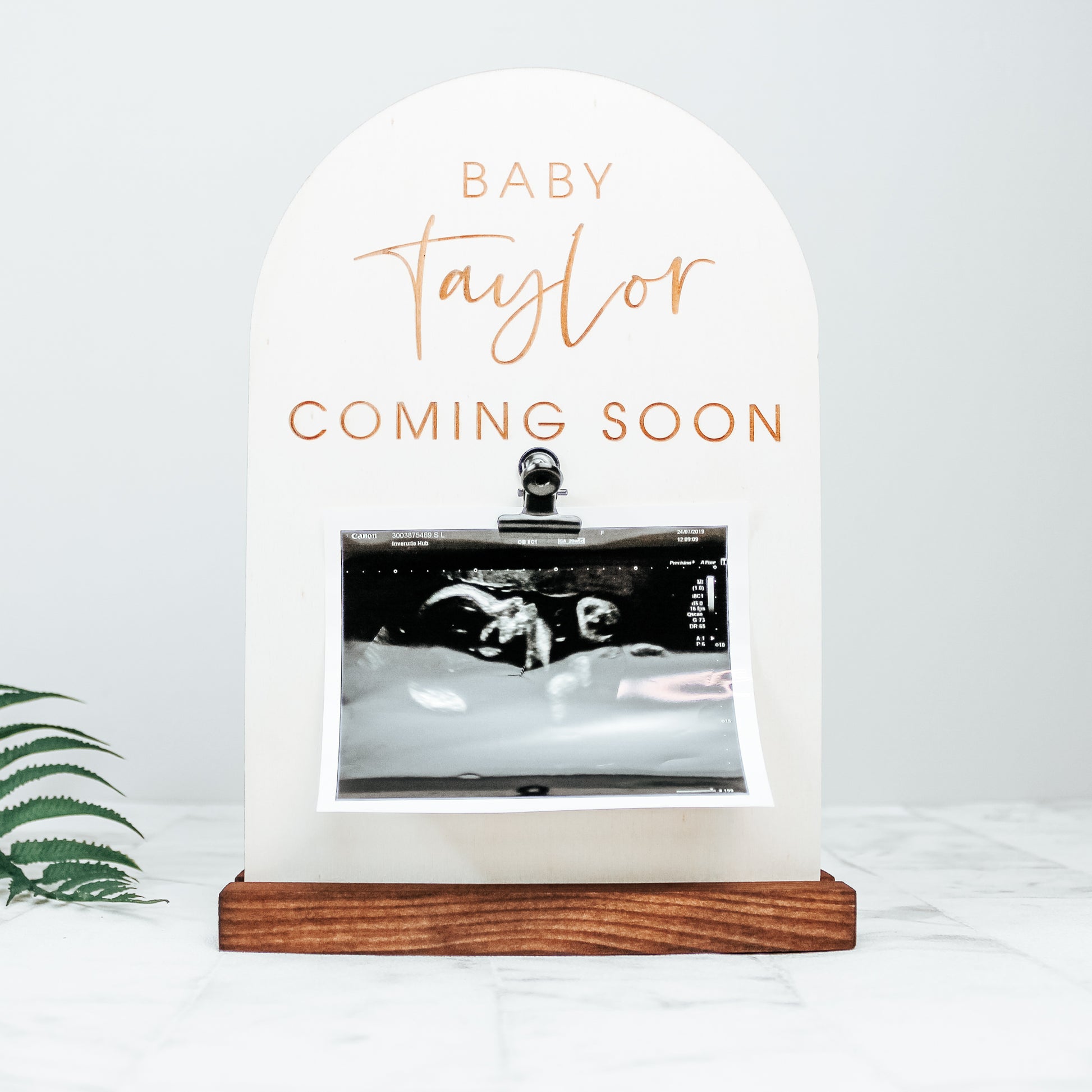 pregnancy announcement sign photo prop for instagram. The sign is wooden and is engraved with baby surname coming soon and has a baby scan picture affixed to to it by a clip