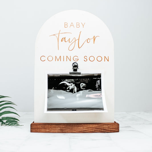 pregnancy announcement sign photo prop for instagram. The sign is wooden and is engraved with baby surname coming soon and has a baby scan picture affixed to to it by a clip