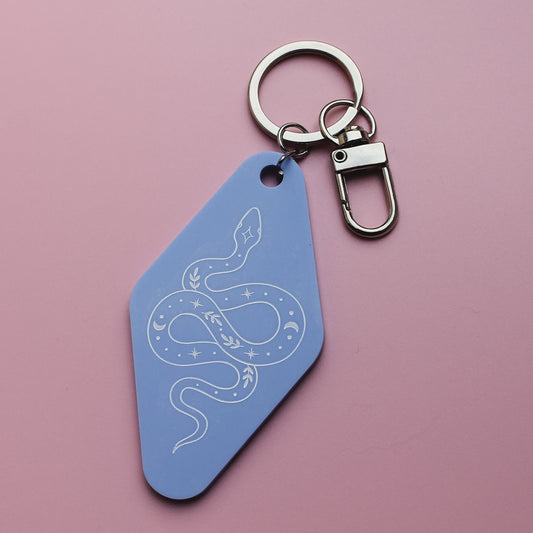 Blue motel style keychain with a celestial snake design on a pink background
