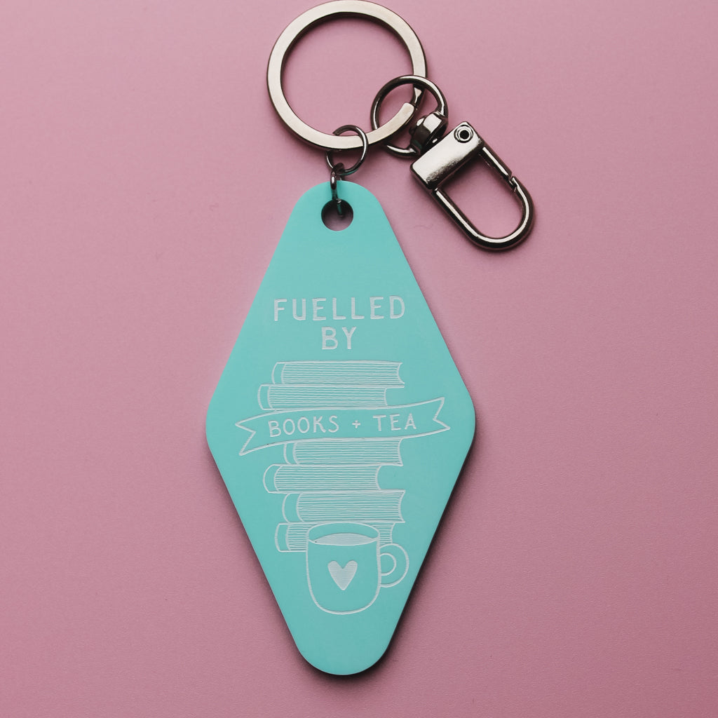 Teal motel style keychain with 'Fuelled by Books + Tea' text on a pink background