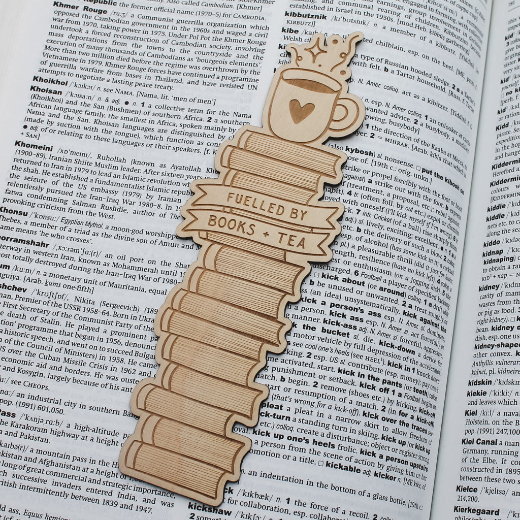 Wooden bookmark shaped like a stack of books with a heart on a tea cup, placed on an open book.