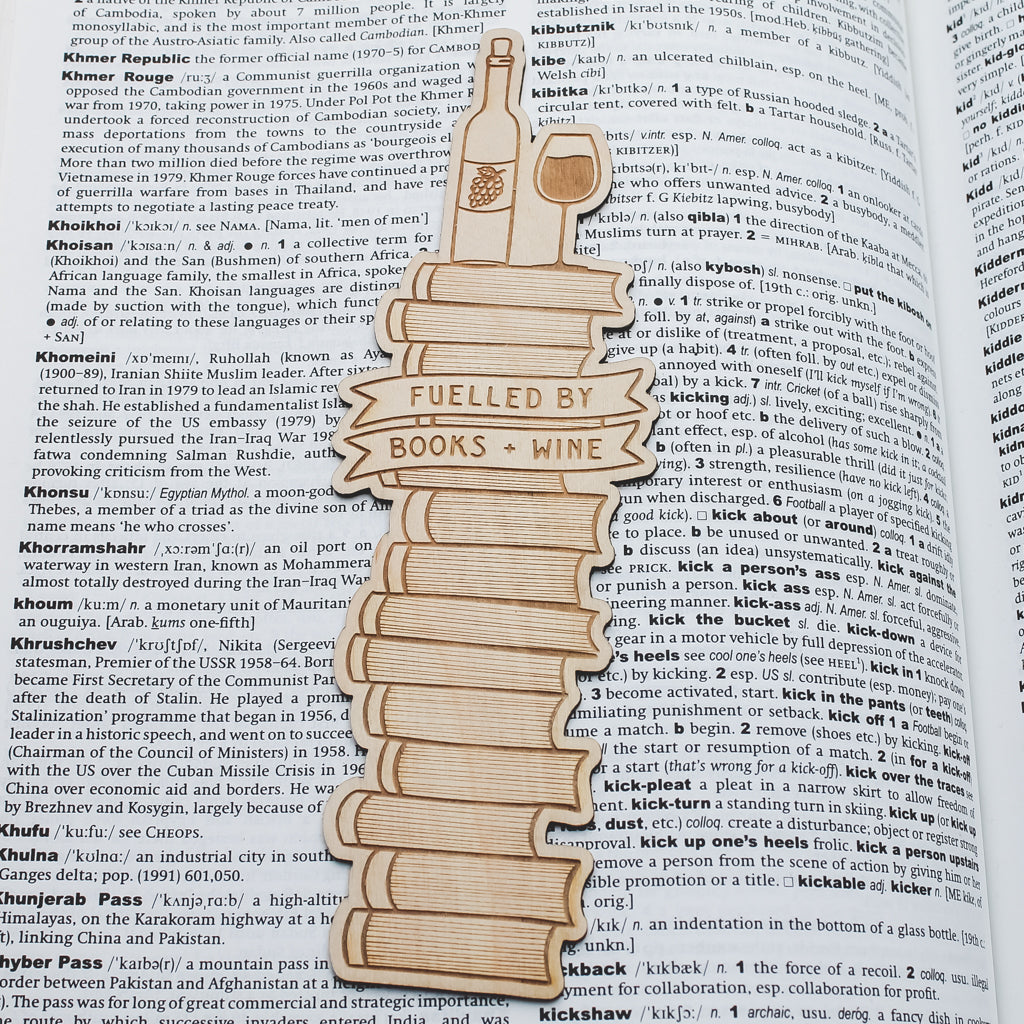 Wooden bookmark shaped like a bottle and glass with 'Fuelled by Books & Wine' text on an open book page.