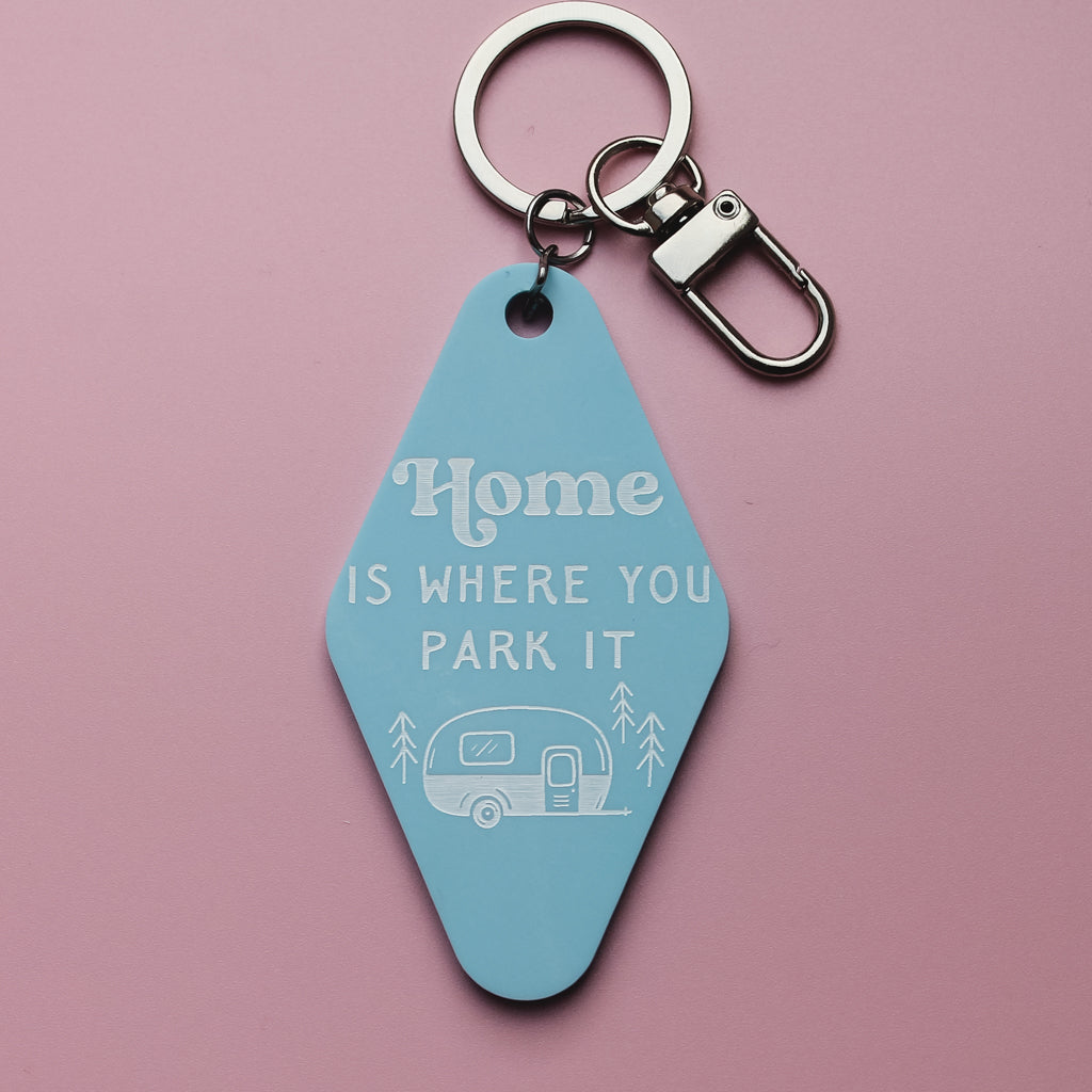Blue motel style keyring tag with 'Home is where you park it' text and caravan illustration on a pink background