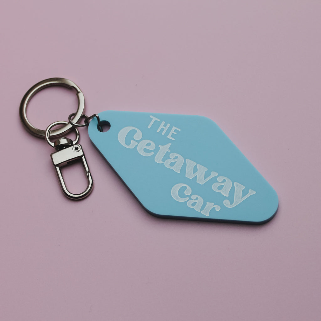 Blue motel style keychain tag with 'The Getaway Car' text on a pink background