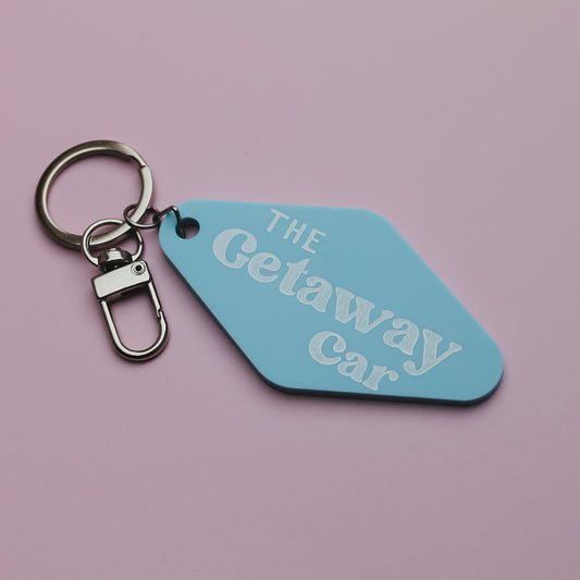 Blue motel style keychain tag with 'The Getaway Car' text on a pink background