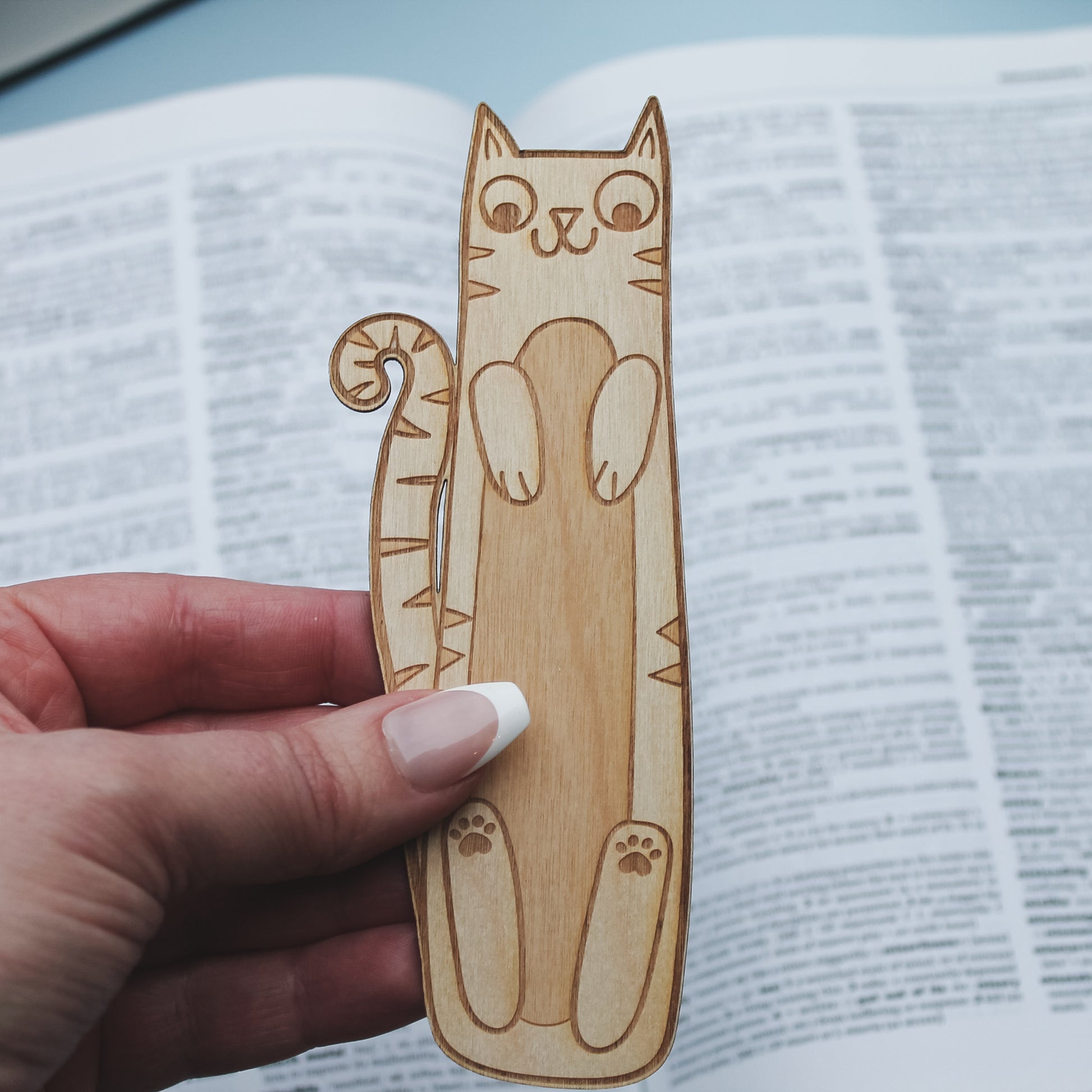 Wooden cat-shaped bookmark held over an open book