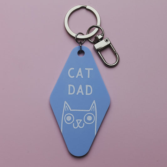 Blue Motel Style keychain with 'Cat Dad' text and cat illustration on a pink background