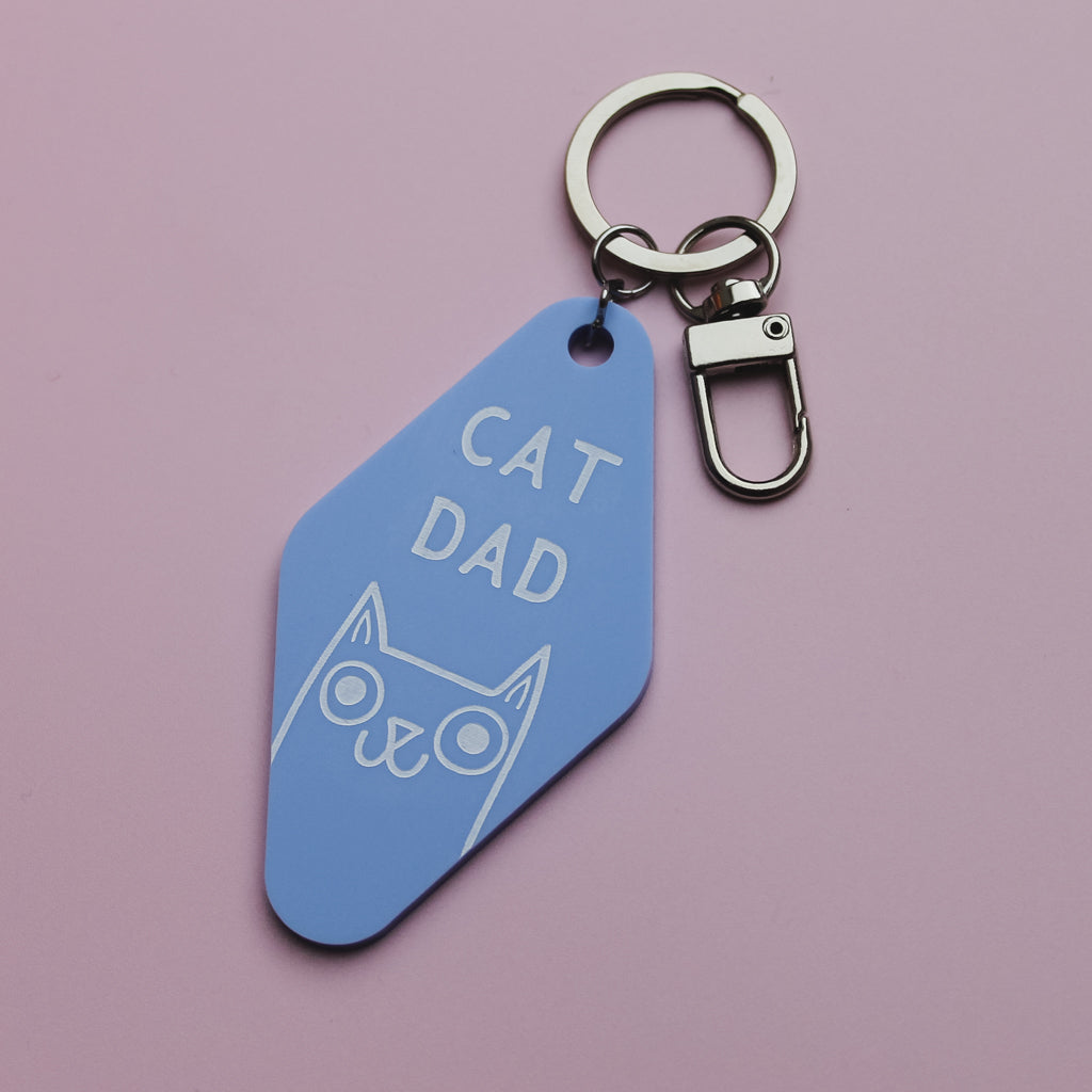 Blue Motel Style keychain with 'Cat Dad' text and cat illustration on a pink background