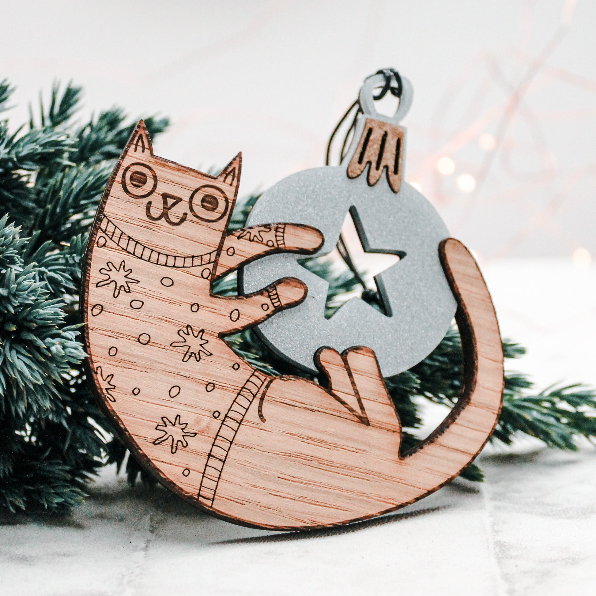 wooden christmas cat in a festive star jumper playing with a silver Christmas bauble decoration.