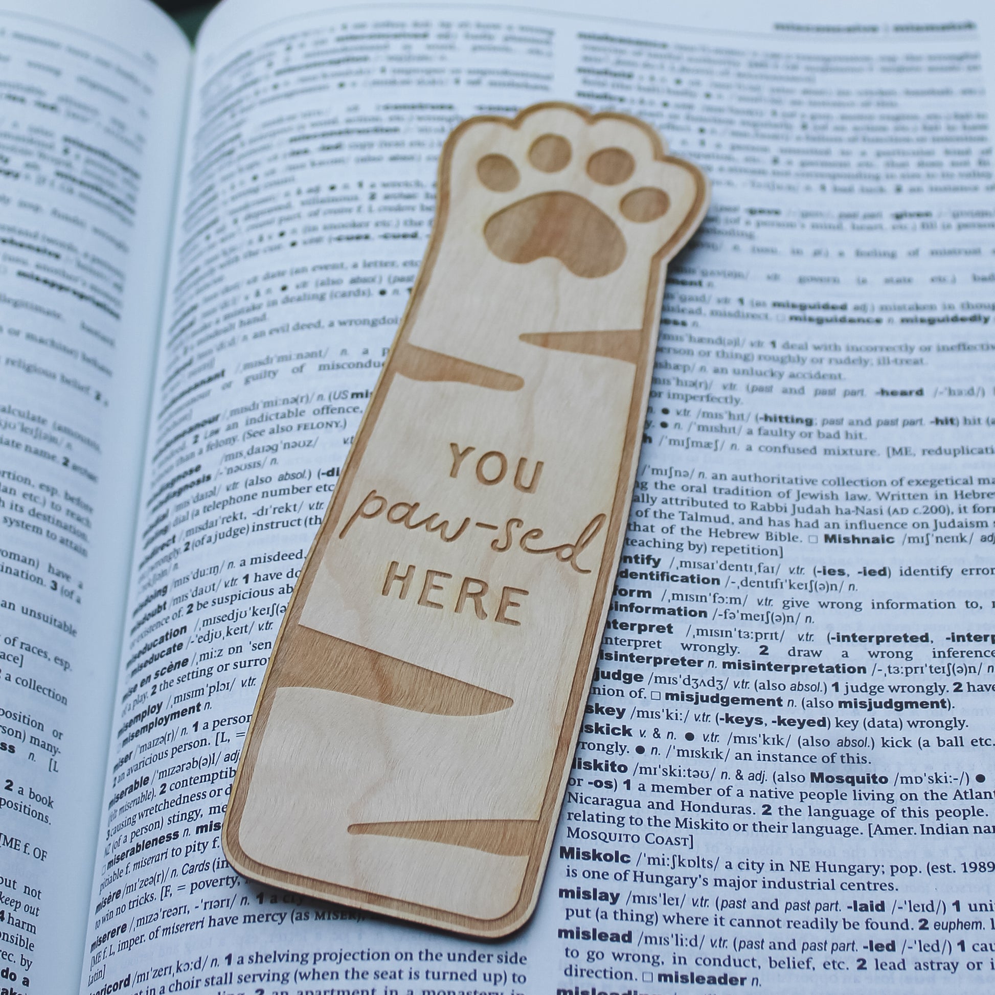 Wooden bookmark with paw design and 'You paw-sed here' text engraved onto it, sitting on an open book.