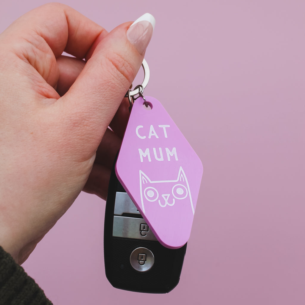 Motel Style Keychain with 'Cat Mum' tag held by a hand against a pink background