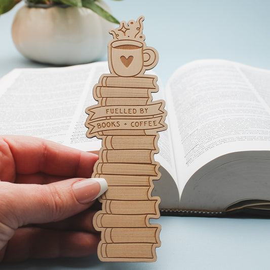 Wooden bookmark shaped like a stack of books and a coffee cup, held over an open book.