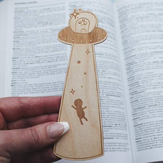 Wooden bookmark with engraved alien / UFO design design held over an open book