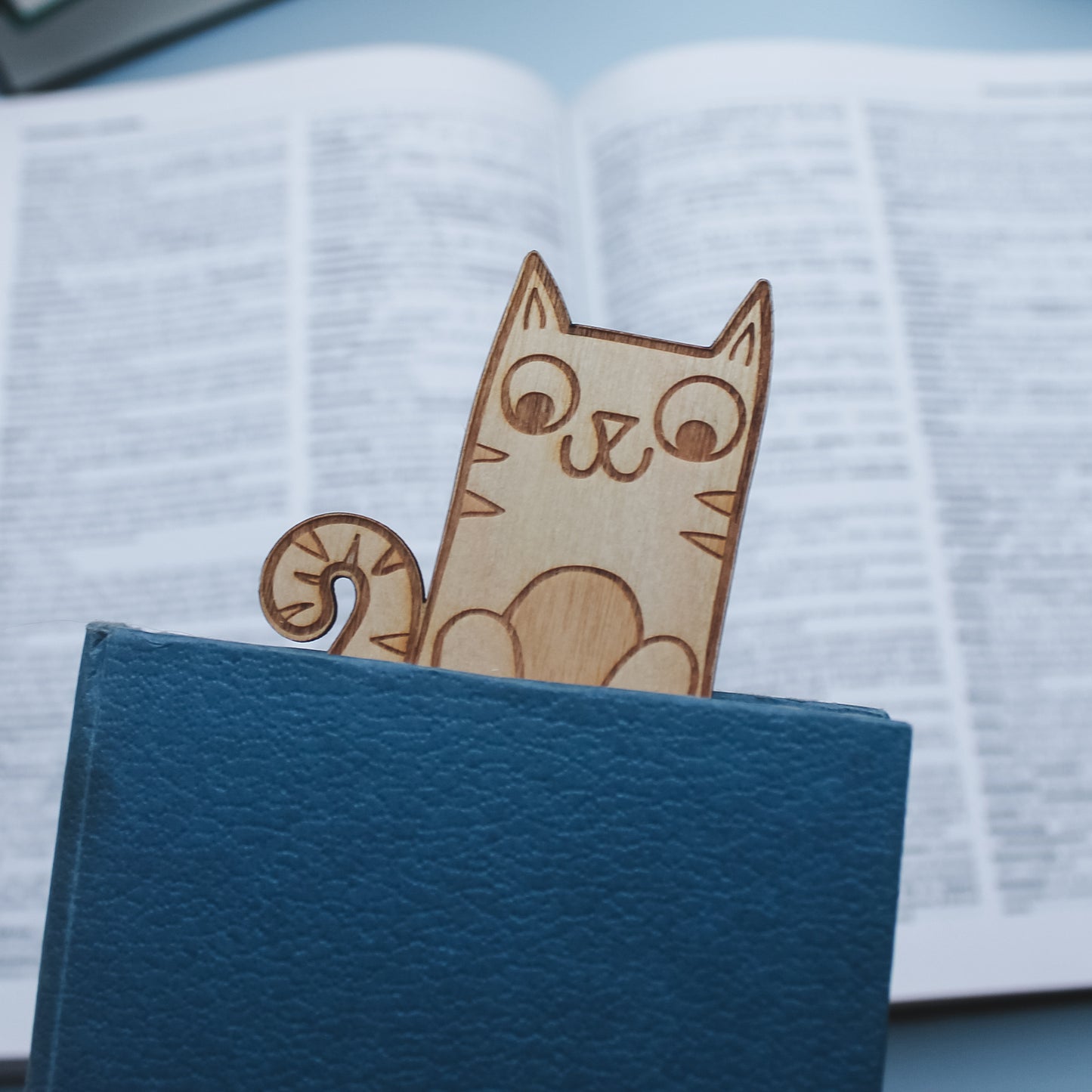 Wooden cat-shaped bookmark peeking out of a closed book 