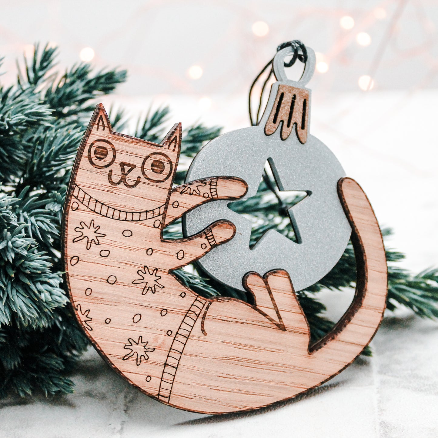wooden Christmas cat in a festive star jumper playing with a silver Christmas bauble decoration.