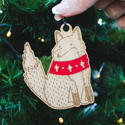 wooden fox in winter scarf Christmas decoration held in front of a Christmas tree 

