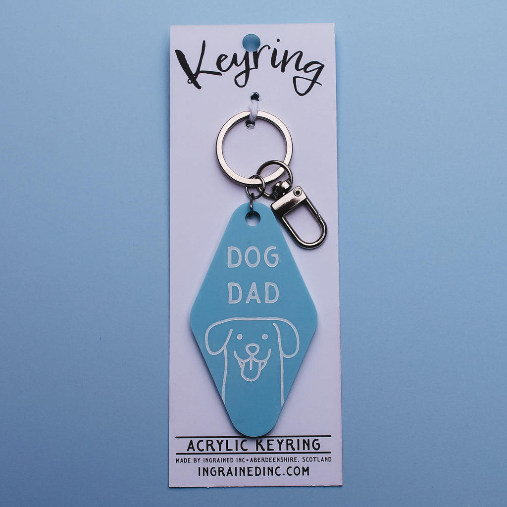 Blue Motel Style keychain with 'Dog Dad' text on a white backing card against a blue background