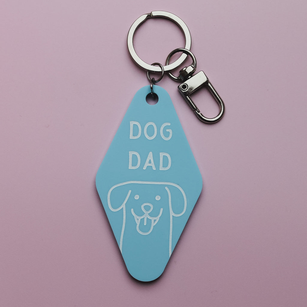 Blue Motel Style keychain tag with 'DOG DAD' text and dog illustration on a pink background