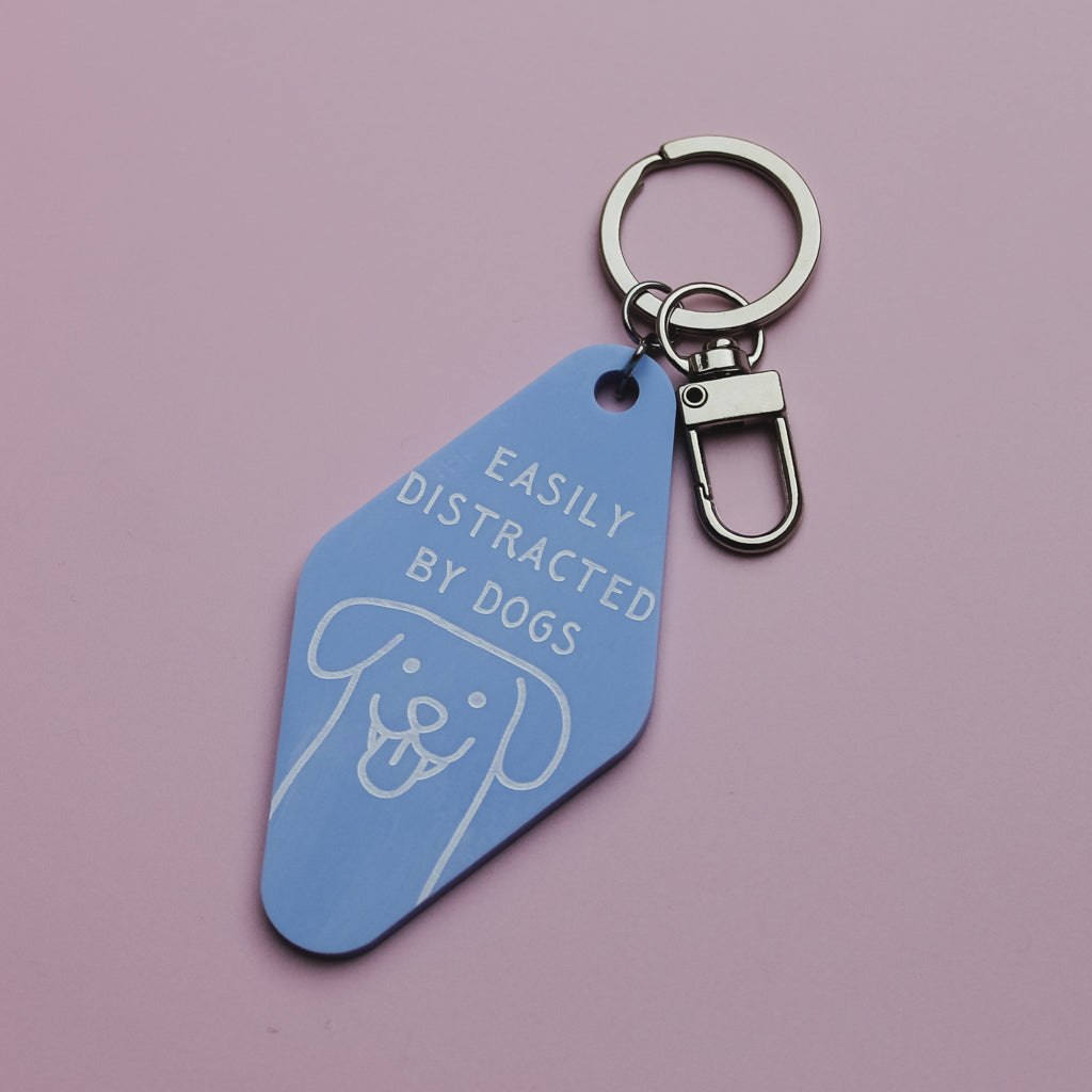 Blue motel style keychain with 'Easily Distracted by Dogs' text on a pink background